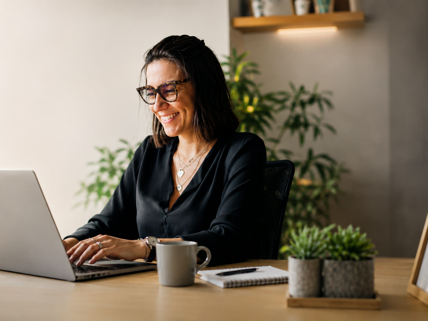Mulher sorrindo enquanto trabalha no notebook em um escritório claro e organizado